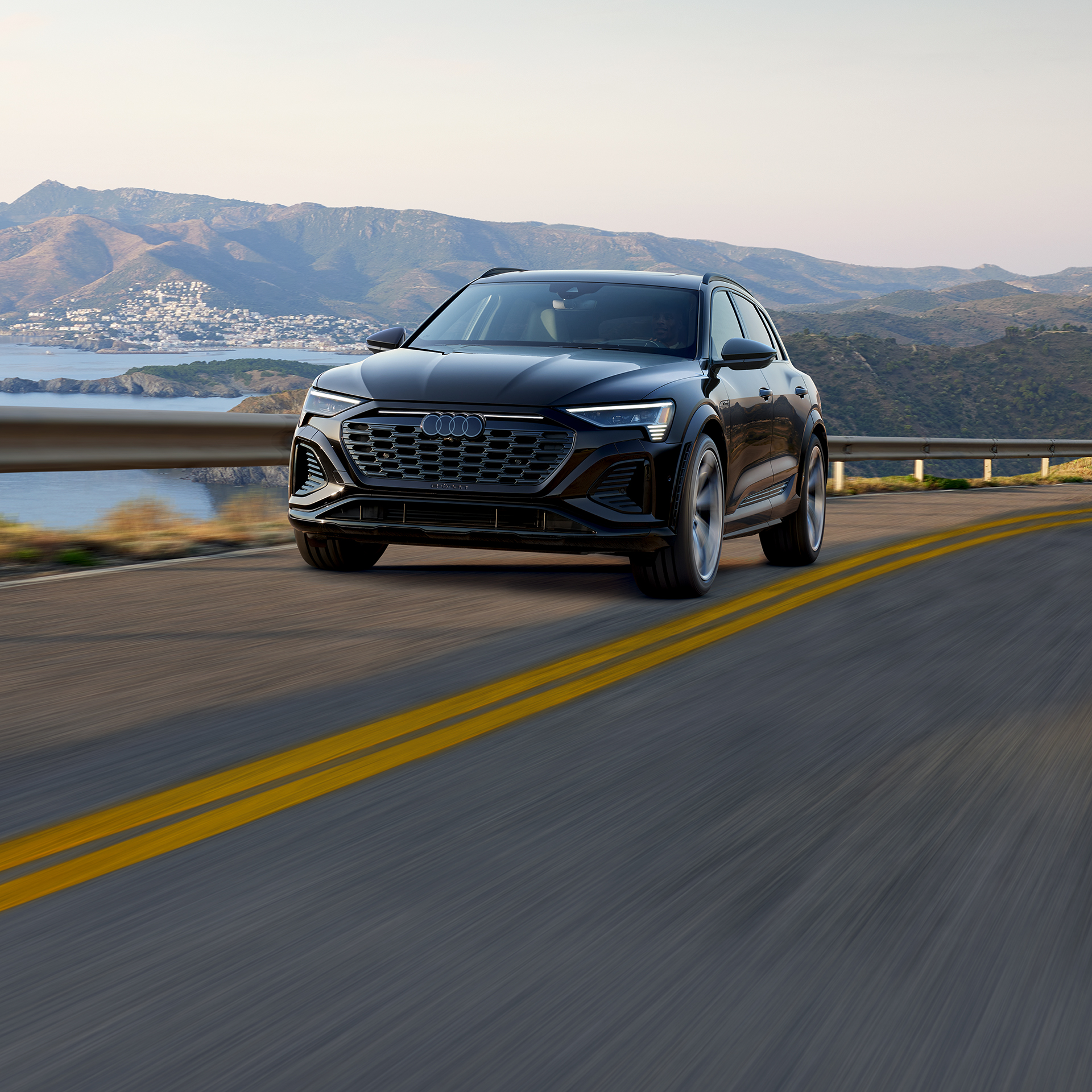 Plan avant de trois quarts d’un Audi SQ8 e-tron noir qui accélère sur une route au bord de la mer.