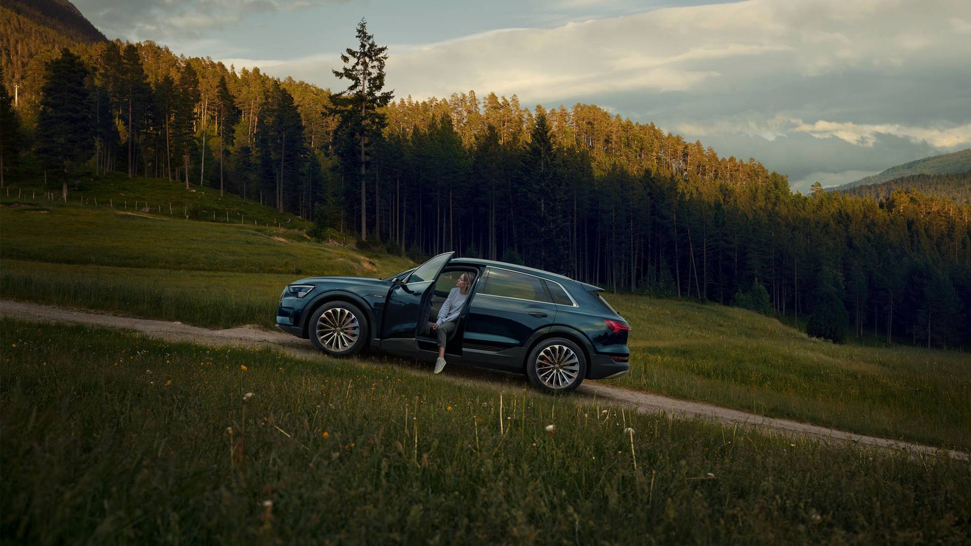 A woman exiting her Audi Q5 on a forested road. 