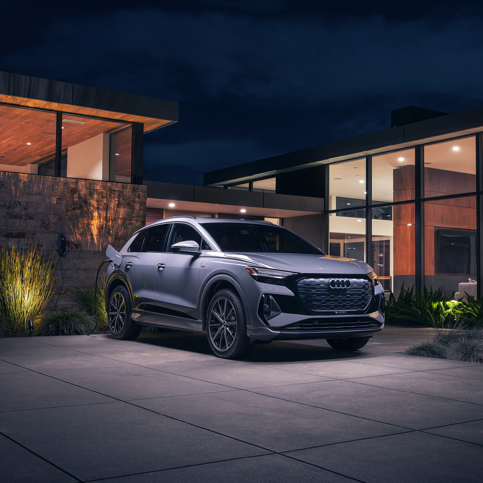 Side profile of a gray Audi Q4 e-tron parked accelerating on a city bridge.