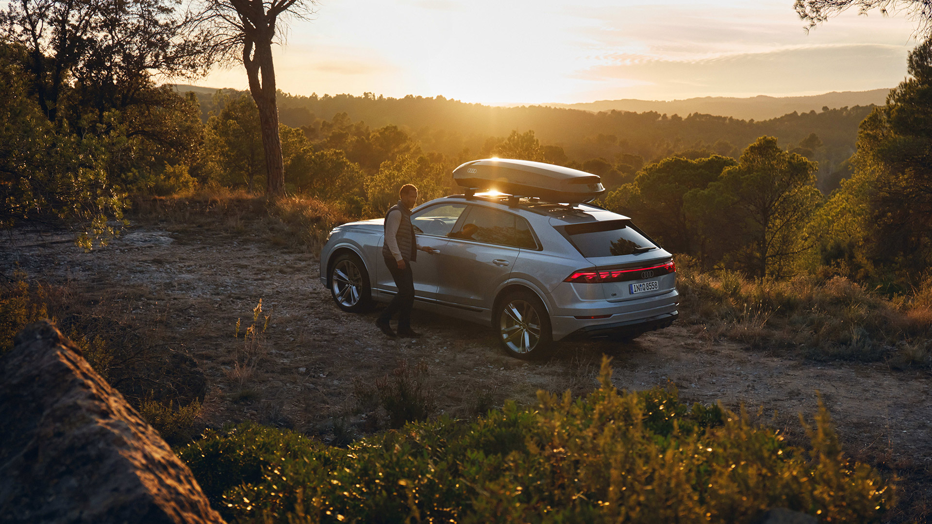 Front 3/4 view of a woman putting a bag on a luggage rack on her Audi vehicle. 