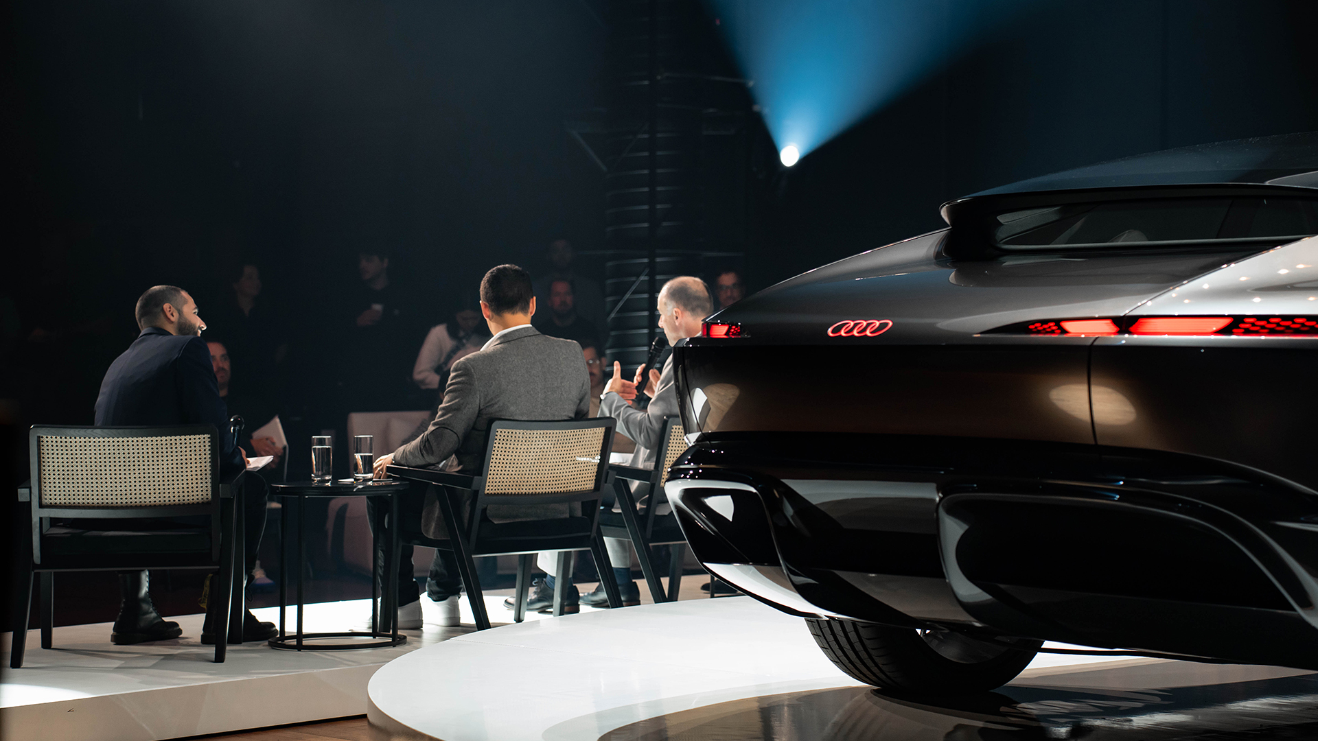 Rear-view of a group of panelists speaking at an Audi House of Progress event.