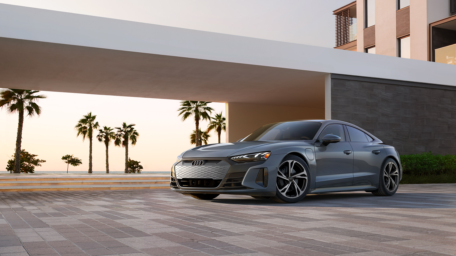 Three-quarter front view of a grey Audi e-tron GT parked in front of a modern house.