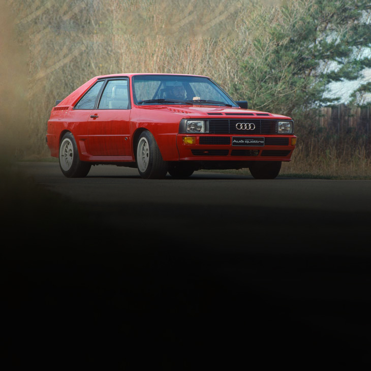 Three-quarter front profile of an older Audi model parked. 