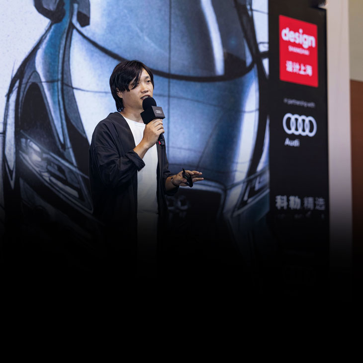 Person speaking on stage with a microphone at the Audi installation at Design Shanghai fair. 