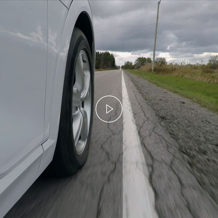 Close-up of the wheel of a white car in motion, nearing the line painted on the road.