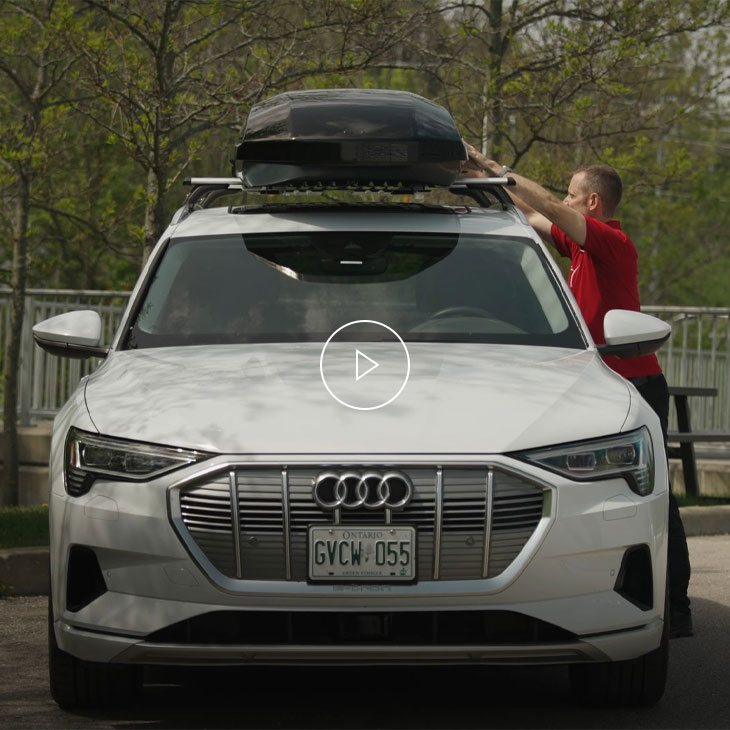 A man in a red shirt attaches his ski and luggage box to the roof of his Audi. 