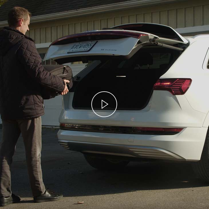  Photo of a person loading a suitcase into the hands-free luggage compartment of an Audi vehicle. 