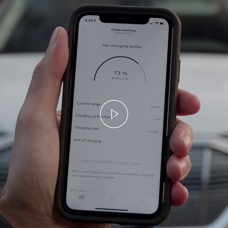 Photo of a person holding a mobile phone displaying the myAudi app charging interface. 