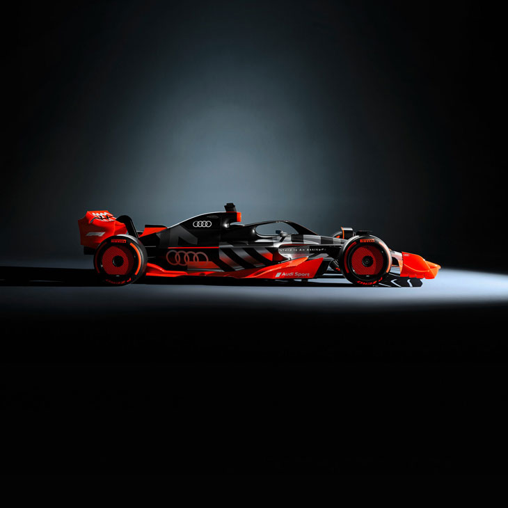 Side profile of an F1 car with Audi livery parked in a darkened showroom.