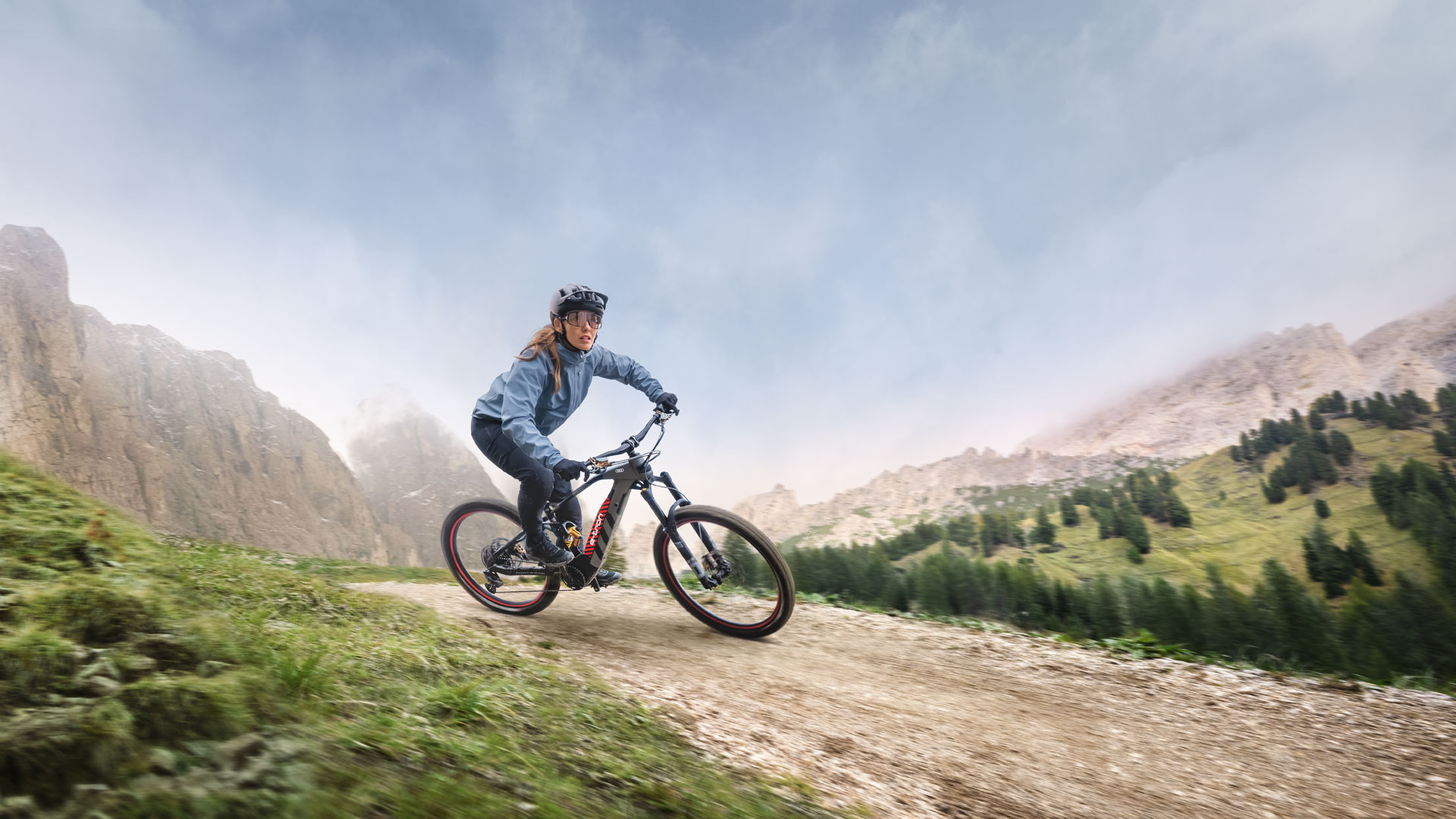 A woman performing a turn with her Audi electric mountain bike, with a mountainous landscape behind. 