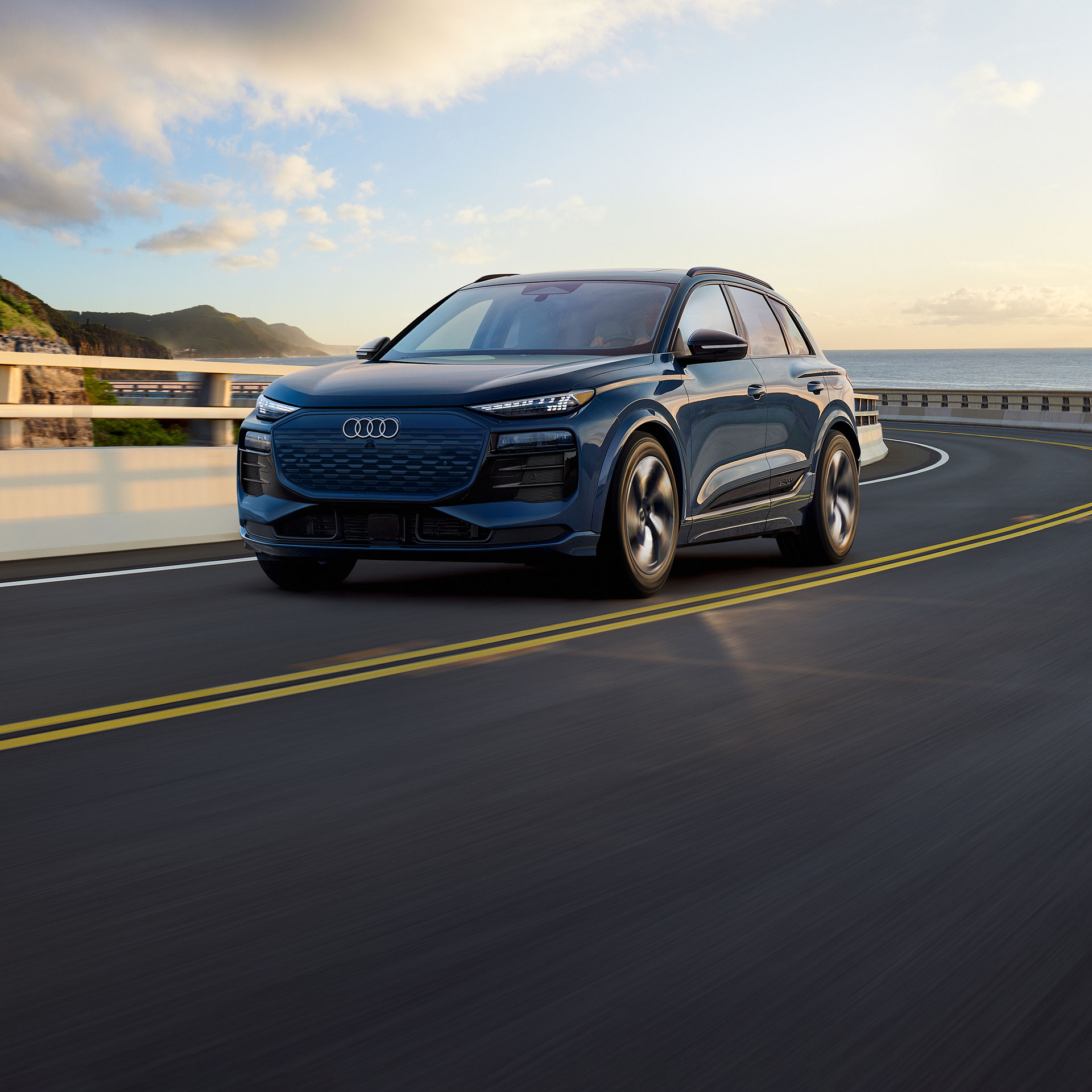 Three-quarter front view of the Audi SQ6 e-tron in motion on an oceanside road.