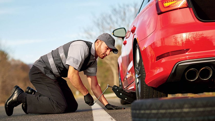 An Audi technician replacing a tire on the side of a road.